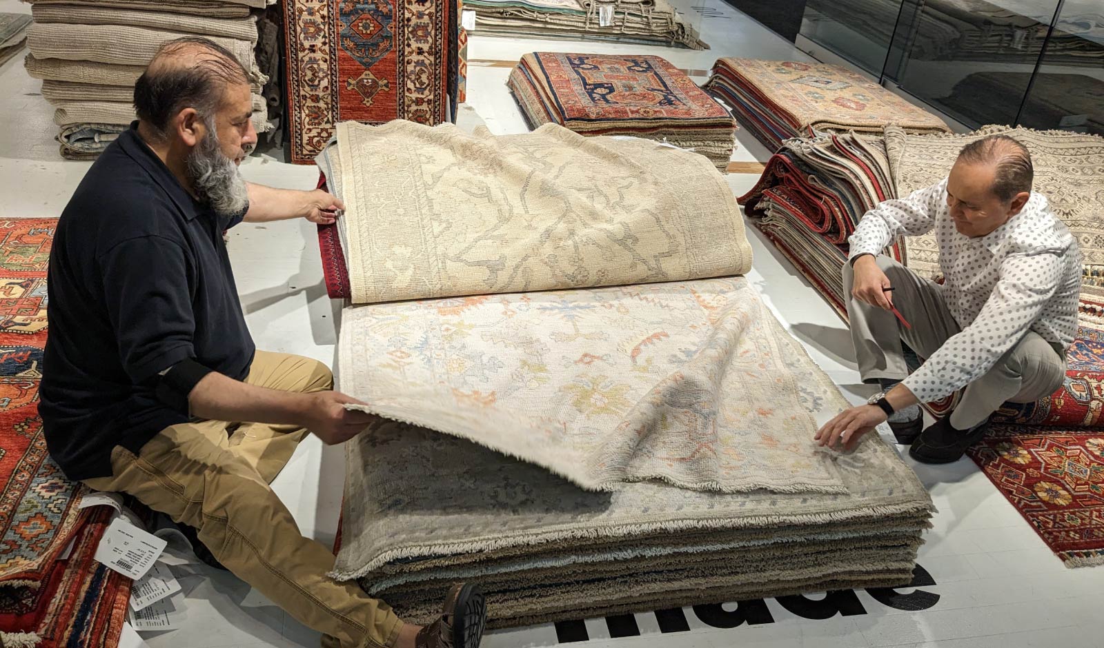 Two men display a stack of woven, Persian-style rugs